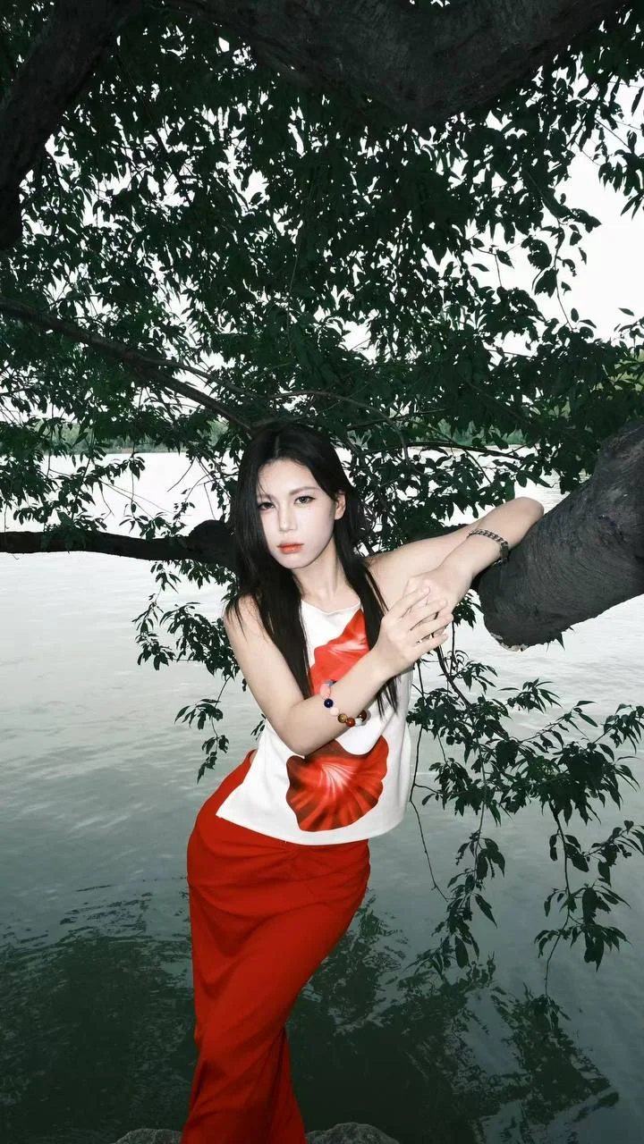 红裙女生靠树枝站在湖边