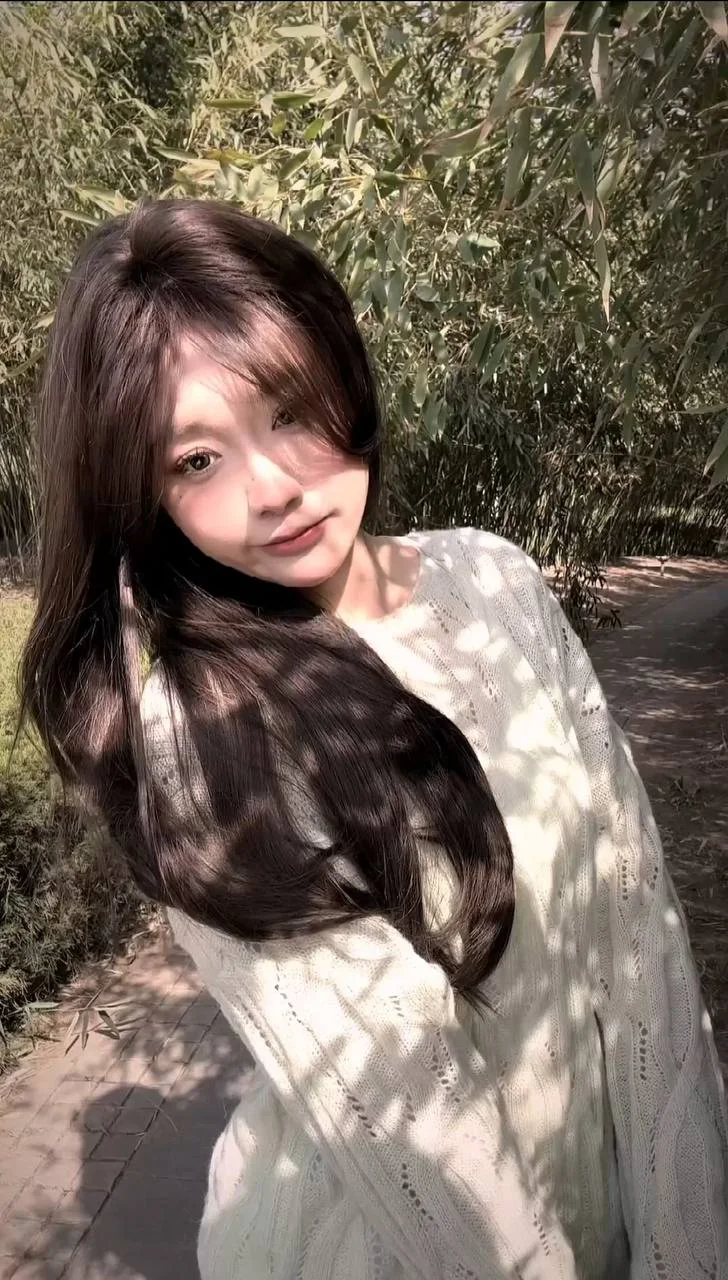 长发女生侧头看镜头，阳光在白毛衣上投下树影