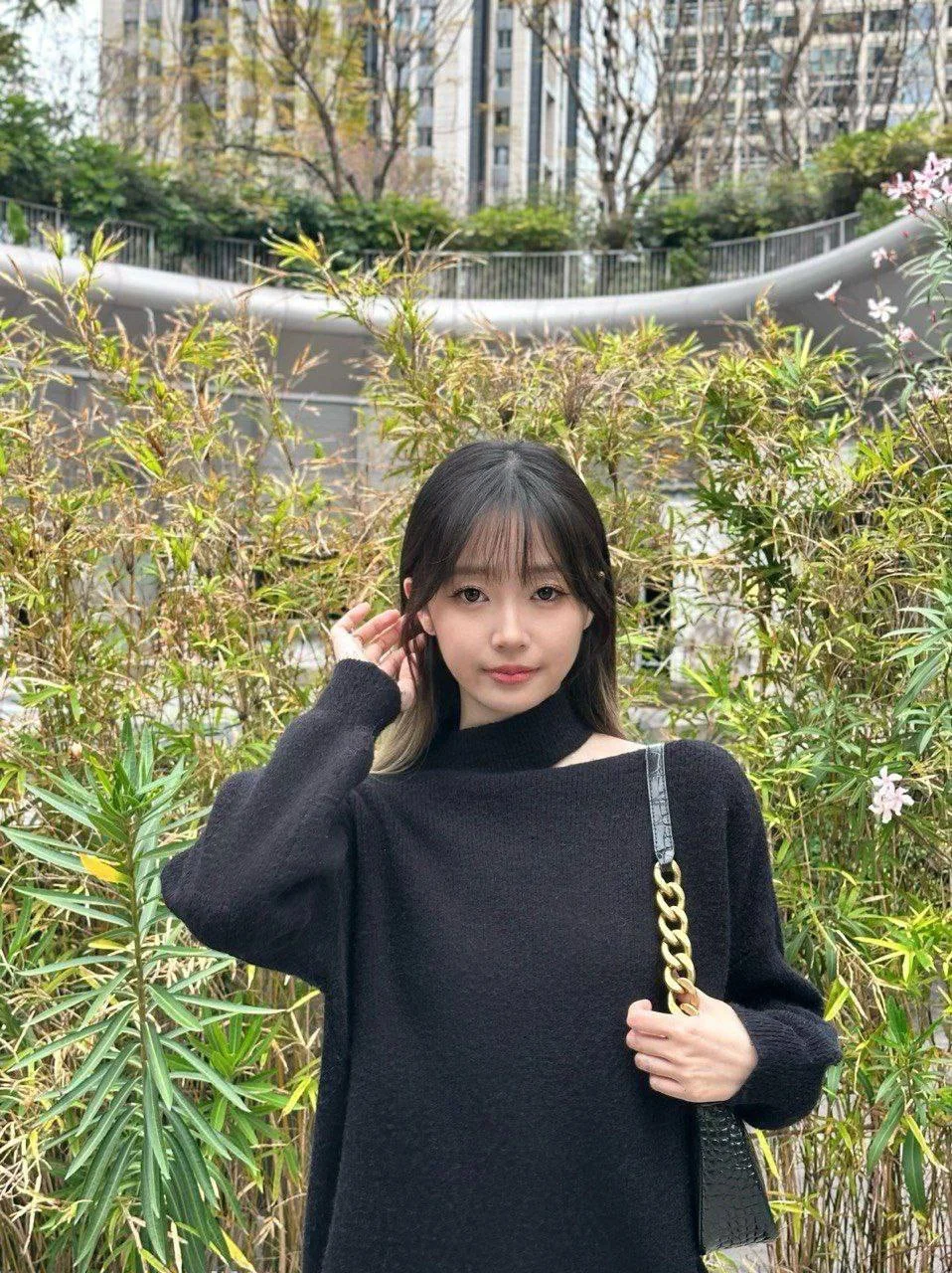 黑毛衣女孩手拿链条包站在竹林前