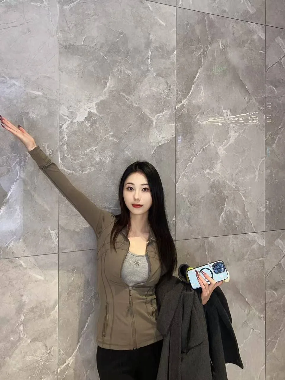 女子靠大理石墙举手机