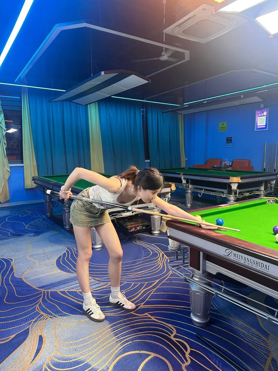 女孩弯腰打台球，手握球杆瞄准蓝球