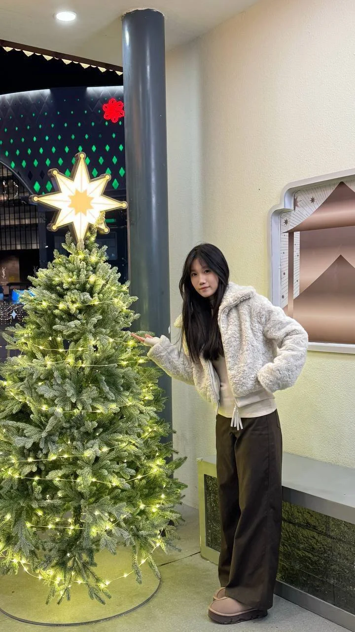女孩站在圣诞树旁指向树顶星星