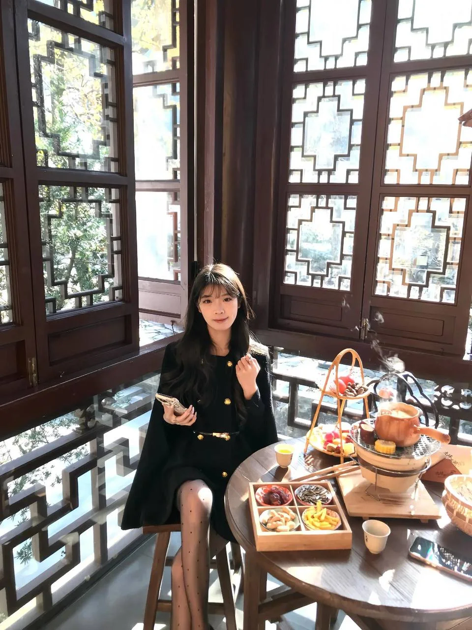 女生坐在中式茶室桌前手拿手机